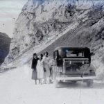 Tre giovani donne in posa di fianco ad un'auto si fanno fotografare lungo un tortuosa strada di montagna negli Anni '30