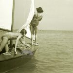 Un bambino e una bambina su una piccola imbarcazione, cercano di districarsi tra cime e vele prima di avventurarsi in mare. Anni '50