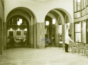 La Galleria dell'OIR a Cesena tra il 1950 e il 1960. In primo piano un cameriere sistema sedie e tavolini del Bar Roma. Sullo sfondo il vecchio palazzo della TIMO