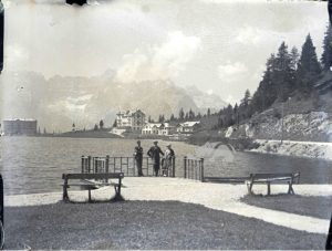 Due signori e una signora sorridenti sul belvedere del lago di Misurina in una estate degli Anni '20. Sullo sfondo le montagne e i primi alberghi
