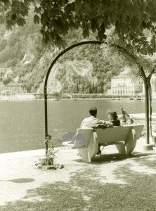 Una coppia conversa su una panchina sulla riva di un lago circondato dal verde negli Anni '50