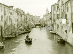 Una piccola imbarcazione a remi attraversa il Canal Vena a Chioggia fra le barche ormeggiate. Siamo negli Anni '50 circa