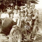 Otto fra bambini e bambine in posa insieme al pilota su un sidecar molto probabilmente in un'aia nel 1919
