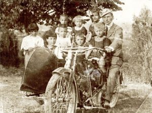 Otto fra bambini e bambine in posa insieme al pilota su un sidecar molto probabilmente in un'aia nel 1919